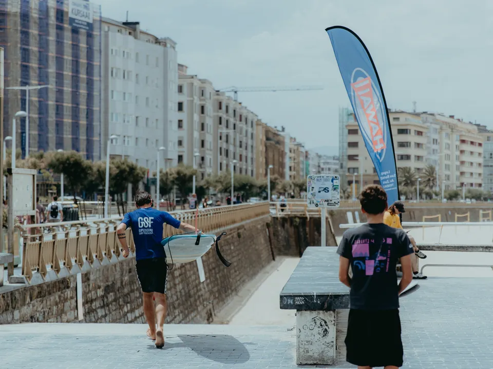 Federazioaren kamisetadun surflaria taula eskuan hondartzara bidean